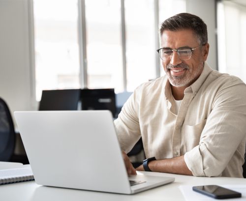 Happy smiling mature Indian or Latin business man ceo trader using computer, typing, working in modern office, doing online data market analysis, thinking planning tech strategy looking at laptop. Happy smiling mature Indian or Latin business man ceo trader using computer, typing, working in modern office, doing online data market analysis, thinking planning tech strategy looking at laptop.